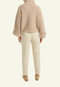 Beige gestrickter Pullover mit hohem Kragen, weiten Ärmeln und gerippter Textur, kombiniert mit cremefarbenen, gerade geschnittenen Hosen und hellbeigen Holzclogs.