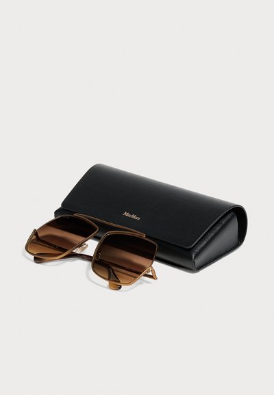 Lunettes de soleil marron à monture carrée avec des accents métalliques dorés à côté d'un étui en cuir noir Max Mara sur un fond clair.
