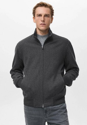 Chaqueta de cremallera gris oscuro con un cuello alto, puños y cintura acanalados. Fabricada con una tela suave, cuenta con bolsillos frontales y un diseño minimalista.