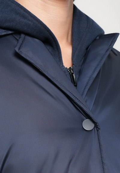 Mornarji modra podložena jakna s kapuco, ki ima gladko, refleksivno teksturo, zapiranje na gumb in kontrastne podrobnosti notranje obloge.