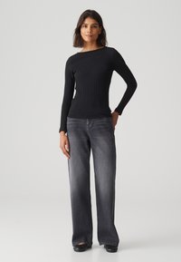 Zwarte geribbelde top met lange mouwen gecombineerd met brede, donkergrijze jeans. De outfit heeft een aansluitend ontwerp en minimale details. Schoeisel is zwart.
