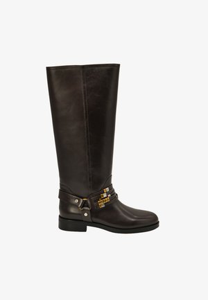 Bota alta de cuero negro con tacón bajo, correas decorativas y adornos metálicos alrededor del tobillo.