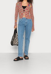 Multikleurige gebreide cardigan met een kraag en knoopsluiting, gecombineerd met lichte denim jeans en zwarte instapsandalen. Inclusief een geweven tas.