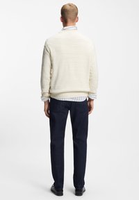 Biały sweter o fakturze z okrągłym dekoltem, noszony na niebiesko-białej koszuli w paski, w połączeniu z ciemnymi spodniami dżinsowymi i czarnymi butami.