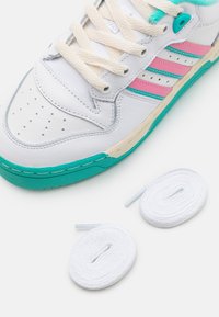 Valkoinen lenkkari, jossa on vaaleanpunaisia ja sinivihreitä yksityiskohtia, nahka- ja synteettisiä materiaaleja, kuvioitu kumipohja ja tasaiset, kermanvalkoiset nauhat sekä lisänä valkoiset nauhat.