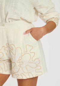 Linnen shorts in off-white, met een gestructureerde stof met een ruitpatroon en gouden borduursels langs de zoom en zakken.