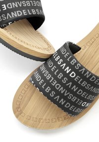 Black slide sandals with patterned fabric strap, featuring white text. Natural wood-like outsole with textured grip and curved shape.