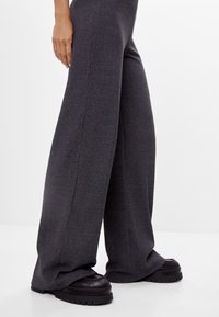 Breda grå ribbade byxor med texturerad yta, kompletterade av kraftiga svarta platåskor. Synliga manschettdetaljer.