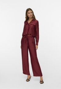 Burgundy satin lounge set with a collared, button-up top featuring two chest pockets, elastic waist pants, and wide-leg design.
