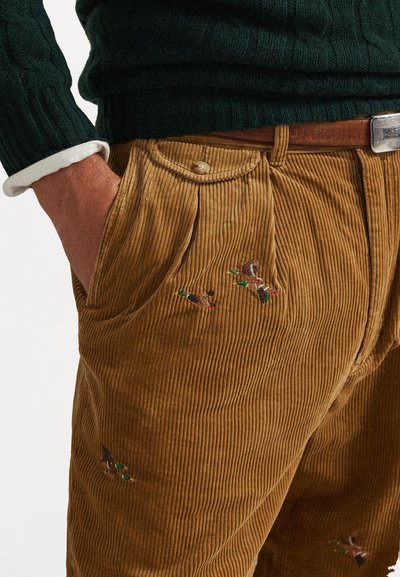 Bruine corduroy broek met verticale ribbels, voorzien van geborduurde eenden in groen en bruin. Klassiek ontwerp met zijzakken en een knoopsluiting in de taille.