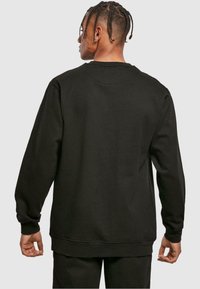 Felpa nera in cotone con maniche lunghe, collo a giro e polsini a costine. Presenta una vestibilità rilassata e una texture liscia, senza motivi visibili.