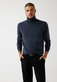 Marineblauer Rollkragenpullover aus weichem Material mit langen Ärmeln, kombiniert mit schwarzen Hosen. Mit gerippten Bündchen und Kragen.