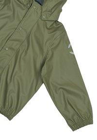 Chaqueta impermeable de color verde oliva con capucha, cierres a presión, puños elásticos y un logo reflectante en la manga izquierda. Textura lisa y brillante.