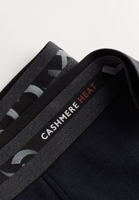 Sorte termoleggings i cashmereblanding med en blød tekstur, der har en grå elastisk talje med teksten "CASHMERE HEAT" i røde og grå accenter.