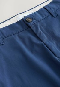 Pantalon bleu marine avec fermeture à boutons à l'avant, passants de ceinture et doublure intérieure visible blanche avec une étiquette de vêtement.