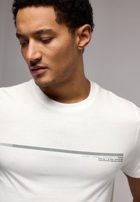 White cotton t-shirt featuring a horizontal gray graphic design with text. Soft texture, crew neck, and short sleeves.