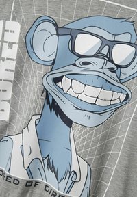 Camiseta gris con un diseño gráfico de un mono azul usando gafas, mostrando una amplia sonrisa. El texto dice "CANSADO DE SUCIO."