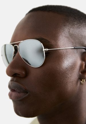 Ochelari de soare stil aviator cu ramă din metal de nuanță argintie, lentile reflectorizante și temple subțiri. Vedere în detaliu care subliniază forma lentilelor și finisajul lustruit.