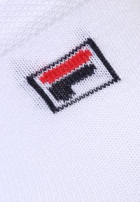 Tissu blanc avec un logo brodé rouge, noir et blanc, comprenant un contour rectangulaire et la lettre "F" stylisée au centre.