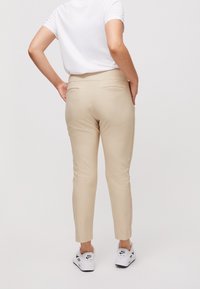 Béžové slim kalhoty s hladkou texturou, ke kotníkům, se zadními kapsami, v kombinaci s bílými teniskami.