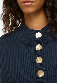 Maglione in maglia a coste blu navy con collo alto e cinque bottoni decorativi dorati a forma di conchiglia lungo la patta. Texture liscia, design aderente.