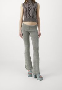 Pletený crop top s kabelovým vzorem v šedých tónech; rozšířené, žebrované kalhoty s knoflíkovými detaily po straně; doplněné o chunky platformové sandály v světle modré.