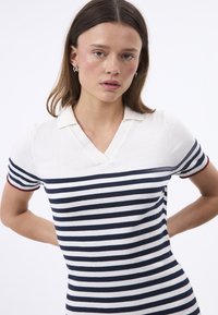 Polo a righe in crema e blu navy, con scollo a V e maniche corte con dettagli rossi. Tessuto morbido con righe orizzontali.