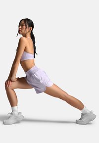 Lys lilla atletisk sports-bh og shorts med afslappet design, blød tekstur, elastisk taljebånd og tætsiddende silhuet, kombineret med hvide sneakers.