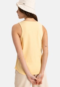D�ébardeur jaune clair en coton doux. Présente un col rond, une conception sans manches et un ourlet incurvé. Coutures minimales, texture lisse.
