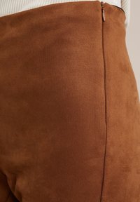 Hnědé kalhoty z umělé broušené kůže s hladkou texturou, vysokým pasem a jemným leskem. Mají postranní zip na zapínání.