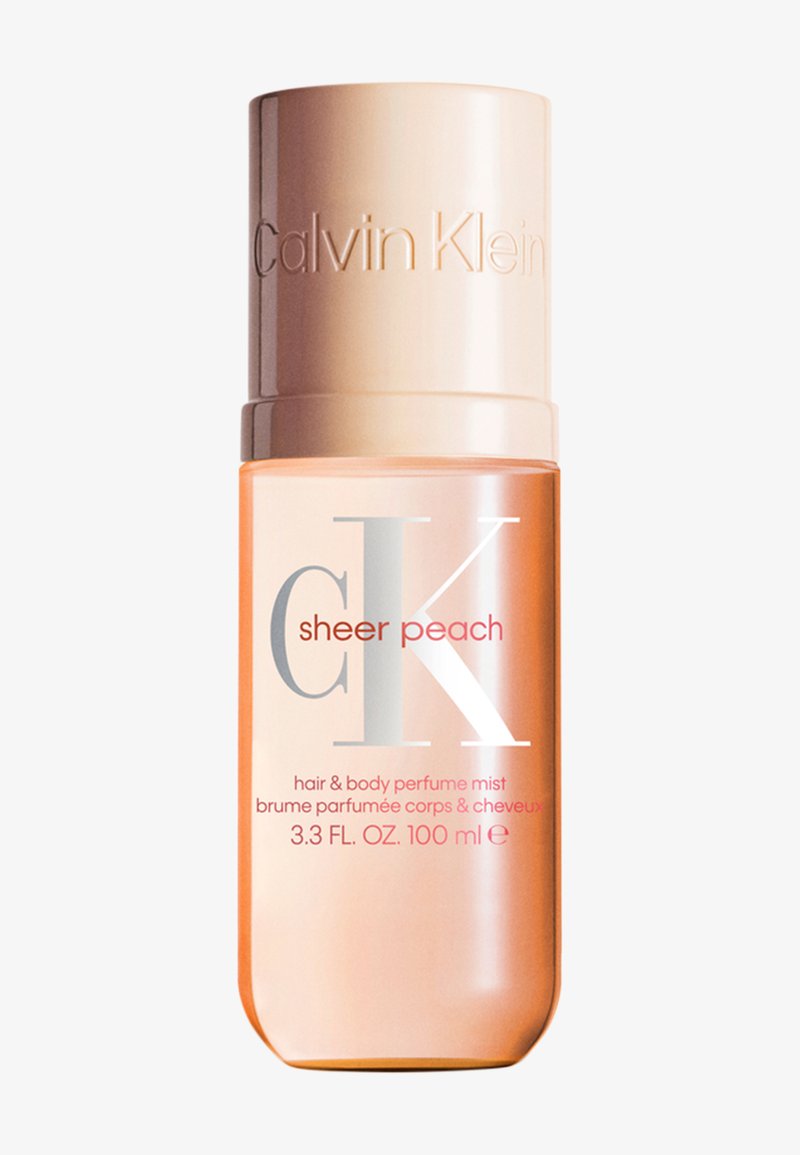 Flacon de parfum brume cheveux et corps Calvin Klein Sheer Peach, 100 ml, avec un bouchon couleur pêche et un liquide pêche translucide à l’intérieur.