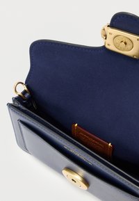 Marineblauwe leren handtas met een suède interieur, gouden hardware, sluiting met gesp en een kaartvak. Kenmerkt zich door een gladde textuur en contrasterende stiksels.