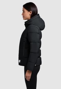 Sort puffervest med hætte, lynlåslommer og quiltet design. Glat tekstur med en tætsiddende silhuet og et logo-patch på kanten.