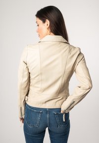 Beige leren motorjack met een getailleerd ontwerp, ritsmanchetten en vormgevende naden. Gepaard met denim jeans.