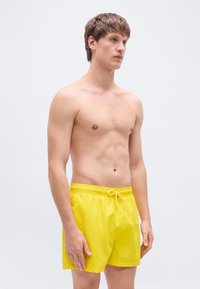 Κίτρινα μαγιό με ελαστική μέση και κορδόνι, κατασκευασμένα από ελαφρύ υλικό, με λεία υφή και κλασικό κοντό σχέδιο.