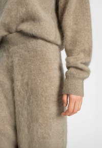 Beige ullblandningstickad tröja med mjuk, ludden textur. Den har en avslappnad passform och ribbade ärmslut, vilket framhäver komfort och värme.