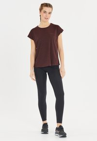 Bordeaux gestreepte top met korte mouwen, gecombineerd met zwarte leggings en zwarte sportschoenen. De top heeft een relaxte pasvorm en een zachte textuur.