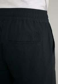 Schwarze Jogginghosen mit einem elastischen Bund, ausgestattet mit einer Gesäßtasche und dezentem Logo-Stick. Hergestellt aus einem glatten, leichten Stoff.