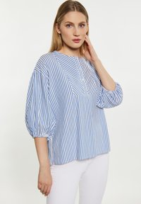 Blusa a righe blu e bianche con scollo rotondo, maniche a sbuffo a tre quarti e taschino frontale. Realizzata in tessuto leggero.