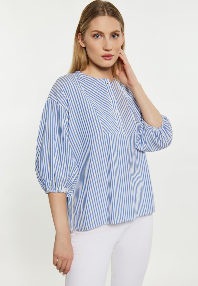 Blusa a righe blu e bianche con scollo rotondo, maniche a sbuffo a tre quarti e taschino frontale. Realizzata in tessuto leggero.