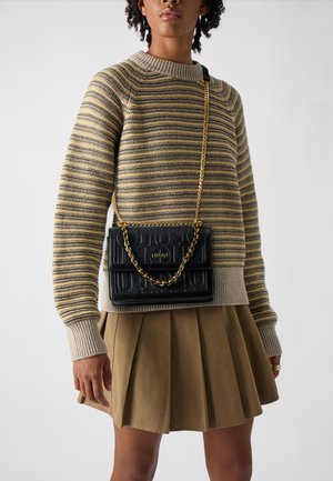 Borsa a spalla in pelle nera con un design testurizzato e una tracolla in catena dorata, abbinata a un maglione a righe in maglia e a una gonna plissettata beige.