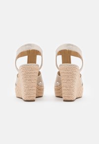 Sandalias de cuña con un tacón de paja texturizada y trenzada. Parte superior de tela beige con un diseño abierto y correa trasera ajustable para mayor soporte.