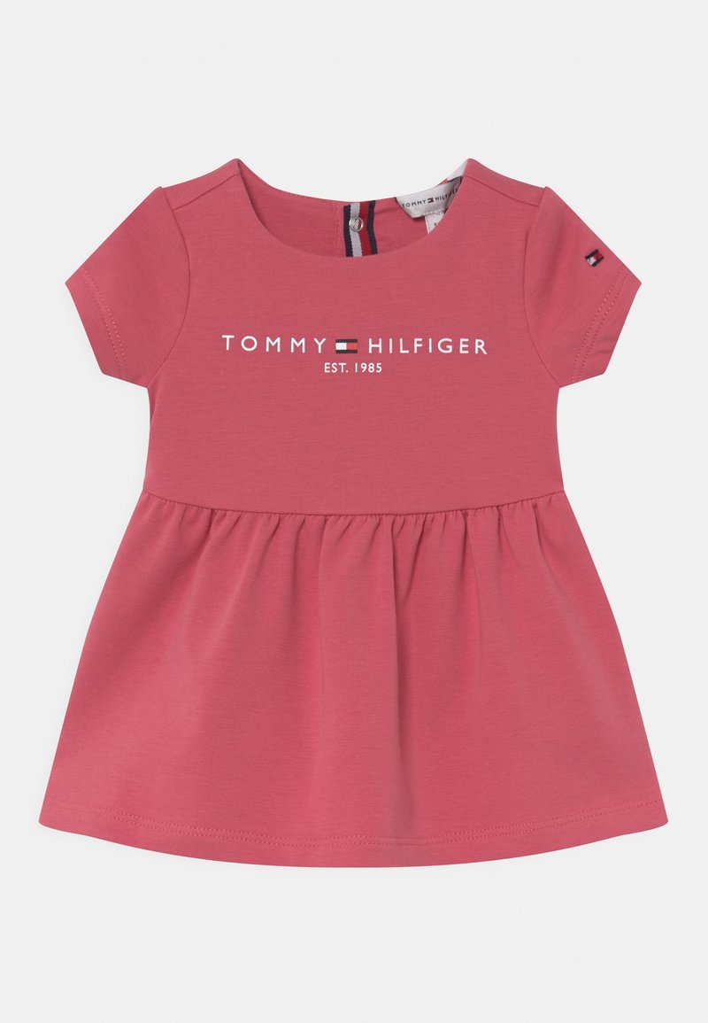 Różowa bawełniana sukienka z krótkim rękawem, z marszczonym dołem, z białym nadrukiem logo "TOMMY HILFIGER EST. 1985" na wysokości klatki piersiowej.