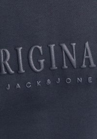 Marineblauwe katoen stof met verhoogde, reliëf tekst: "ORIGINAL" en "JACK&JONES" in een gladde, licht glanzende textuur.