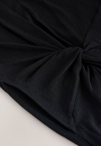 Tela negra torcida en un detalle de nudo, mostrando la textura y las costuras sobre un fondo plano y neutro.