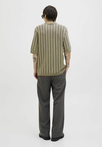 Stribet kortærmet sweater i jordfarver, med en struktureret strik, rund hals og afslappet pasform, parret med mørke, løst siddende bukser.