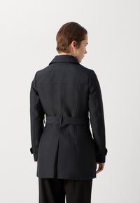 Zwarte jas met een ceintuur in de taille, gestructureerde kraag en lange mouwen. Beschikt over een gladde textuur en achterste naaddetails.