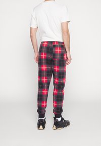 Heren joggers met ruitpatroon in rood, zwart en wit, met een elastische tailleband en cuffed ankles. Gecombineerd met een wit t-shirt en zwarte sneakers.