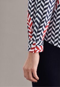 Skjorta med långa ärmar som har ett chevronmönster i röd, marinblå och vit. Knäppt manschett med en mjuk tygkvalitet.