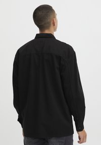 Zwarte langwerpige shirt met lange mouwen van katoen, met een kraag, knoopmanchetten en een rechte zoom. Soepele textuur met een ontspannen pasvorm.